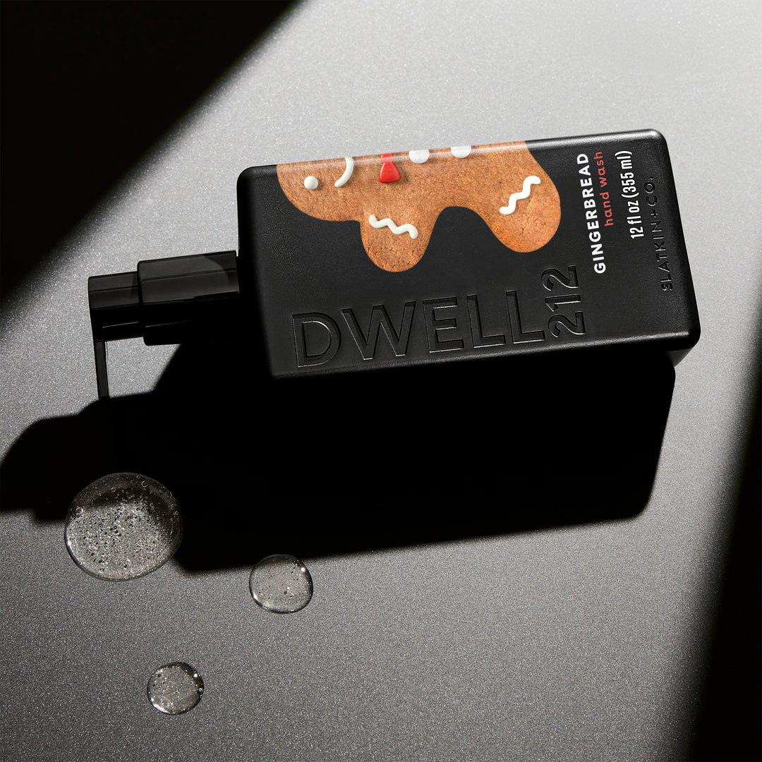 Dwell212 GINGERBREAD hand wash bottle with gingerbread man design laying on its side on a illuminated surface, next to small puddles of dispensed hand wash