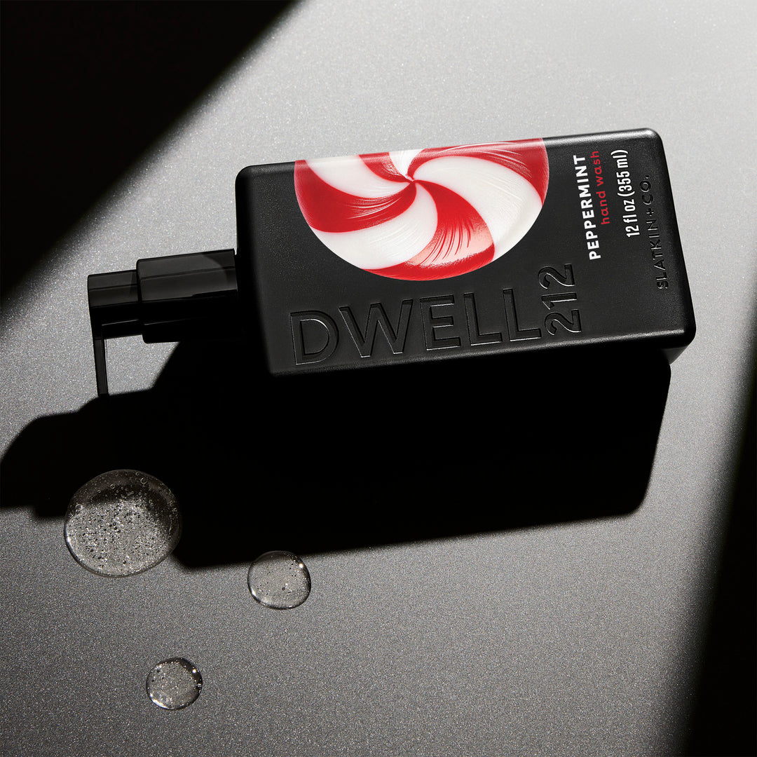 Dwell212 PEPPERMINT hand wash bottle with peppermint swirl design laying on its side on an illuminated surface, next to small puddles of dispensed hand wash