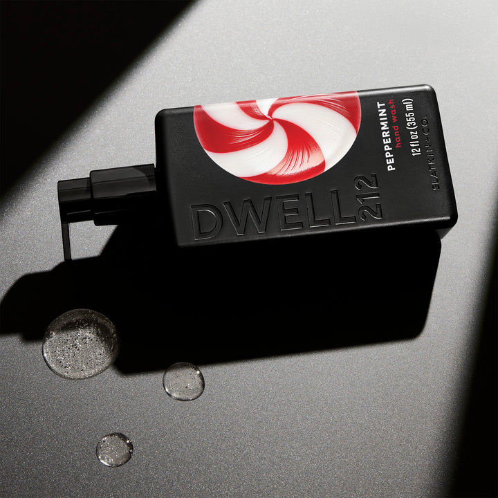 Dwell212 PEPPERMINT hand wash bottle with peppermint swirl design laying on its side on an illuminated surface, next to small puddles of dispensed hand wash
